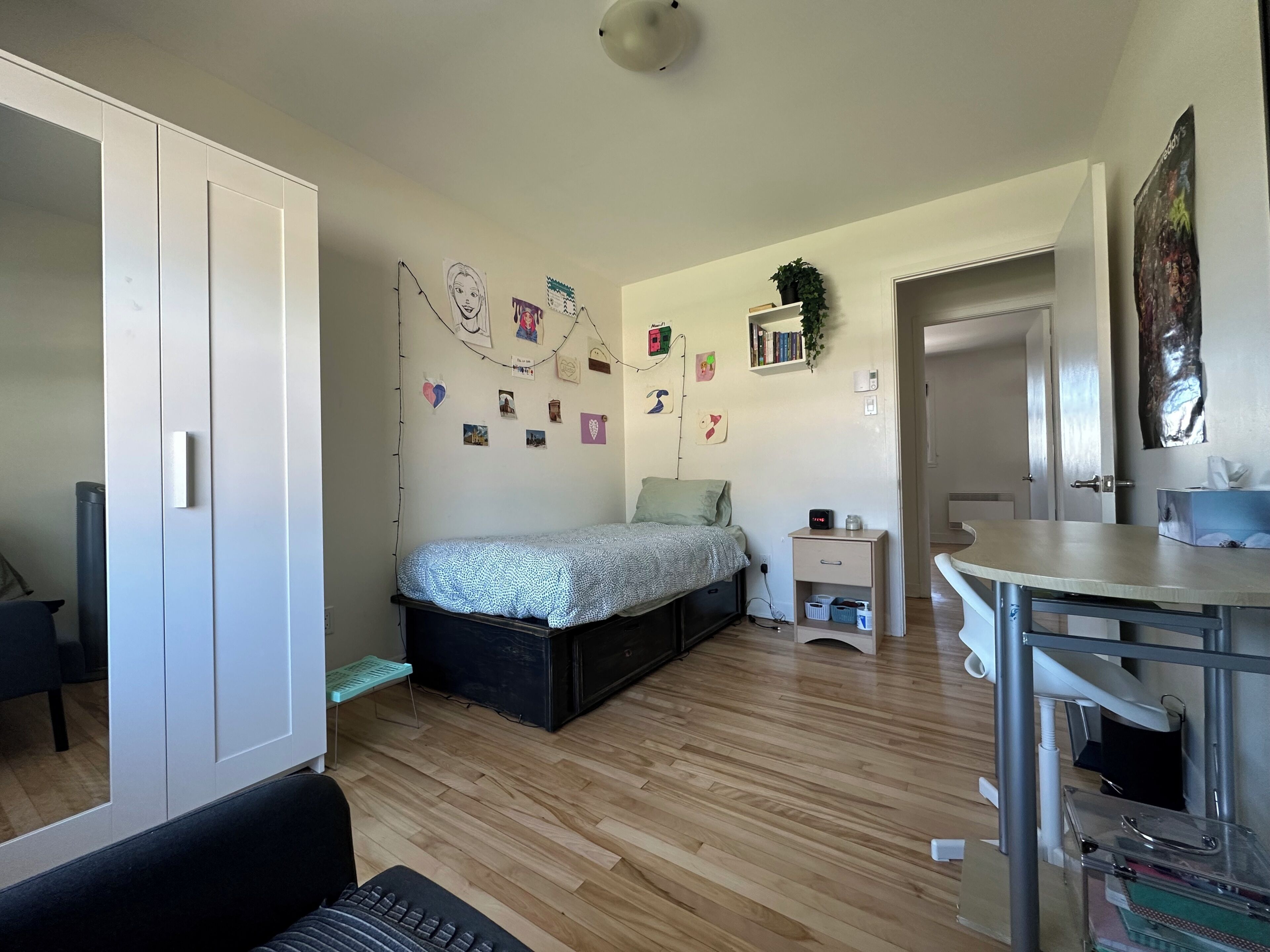 Ein Schlafzimmer mit Bett, Schreibtisch, Kleiderschrank und einer Wand mit Bildern und einem Spiegel.