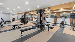 A gym with various exercise equipment, a bench press, and a mirrored wall. - Landing | Chic 1BD, Gym, Game Room (Hyattsville)