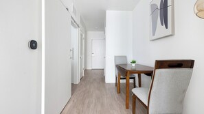 Un couloir qui mène à un espace repas comprenant une table et des chaises en bois, un thermostat et une œuvre d’art encadrée accrochée au mur.