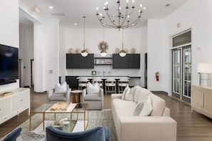 A modern living room with a TV, sofa, and coffee table. There is a kitchen area with cabinets and a dining table. - Landing | Stylish 1BD, Clubhouse, Gym (Bessemer)
