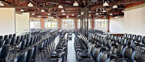 A conference room with rows of black chairs, wooden beams on the ceiling, and large windows.