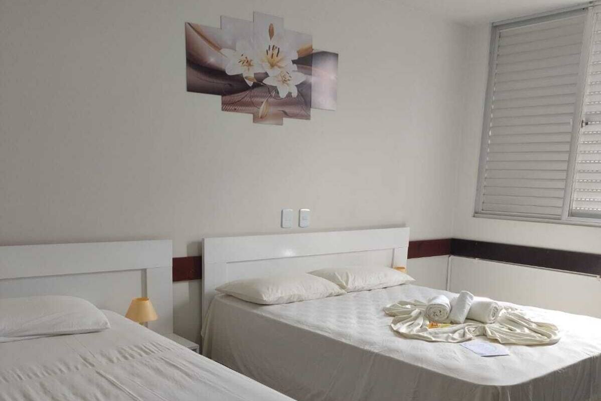 A hotel room with two beds, a wall-mounted artwork, a window with blinds, and a tiled floor.