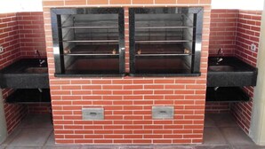 Uma cozinha ao ar livre construída em tijolo, com dois fornos e duas pias.