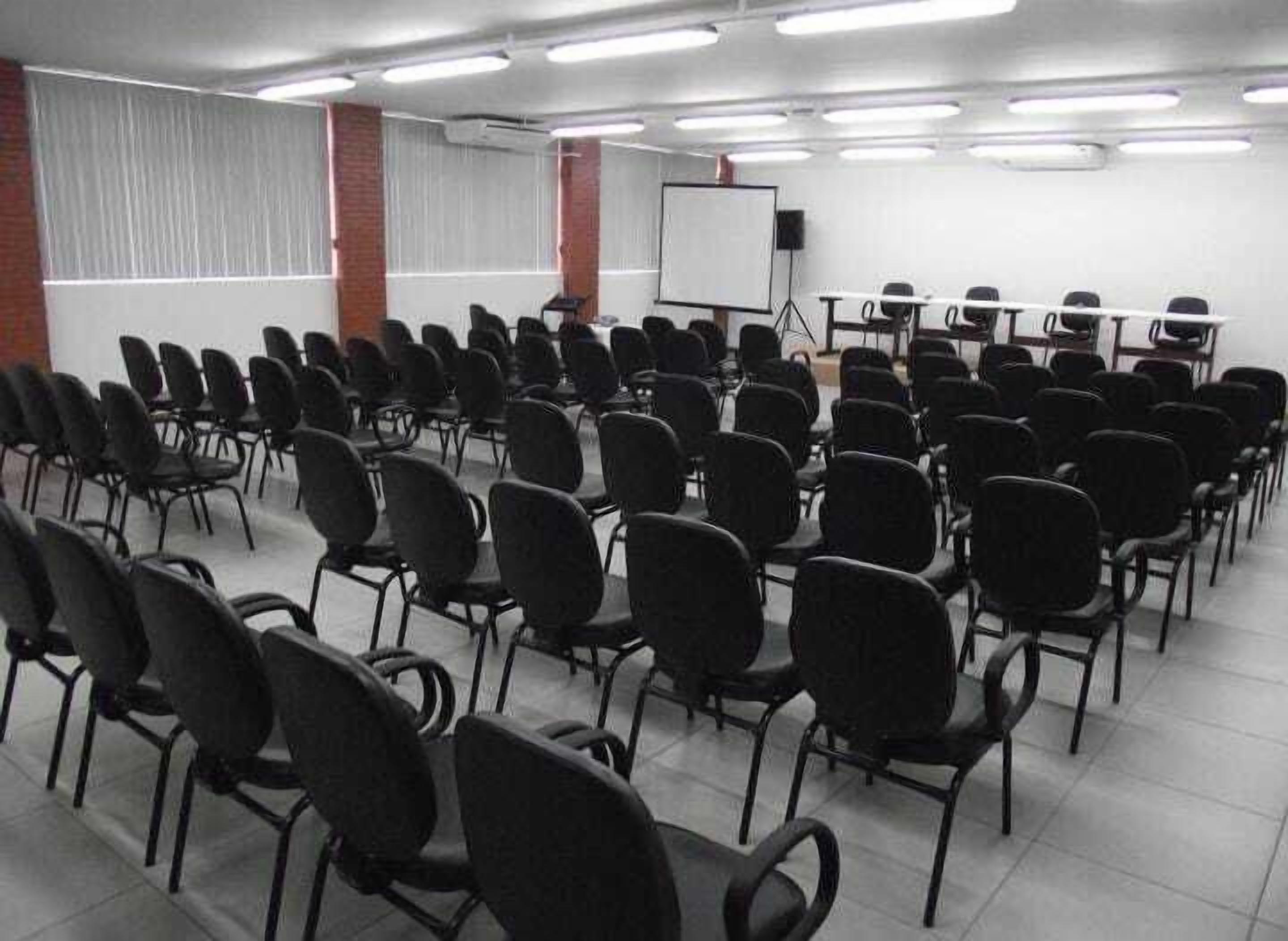 A conference room with rows of chairs, a whiteboard, and a projector screen.
