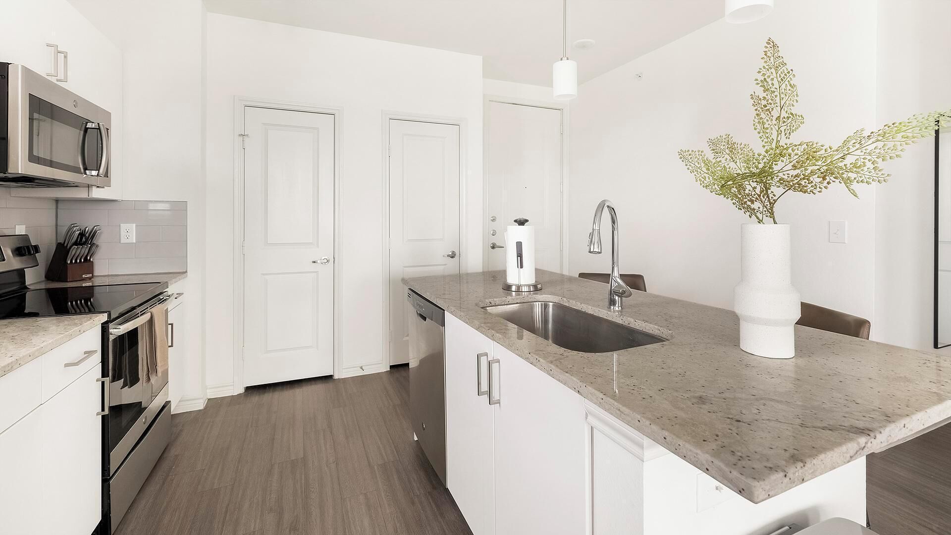 A modern kitchen with a granite countertop, stainless steel appliances, and a white vase with greenery.