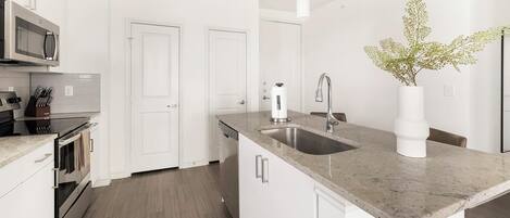 A modern kitchen with a granite countertop, stainless steel appliances, and a white vase with greenery.