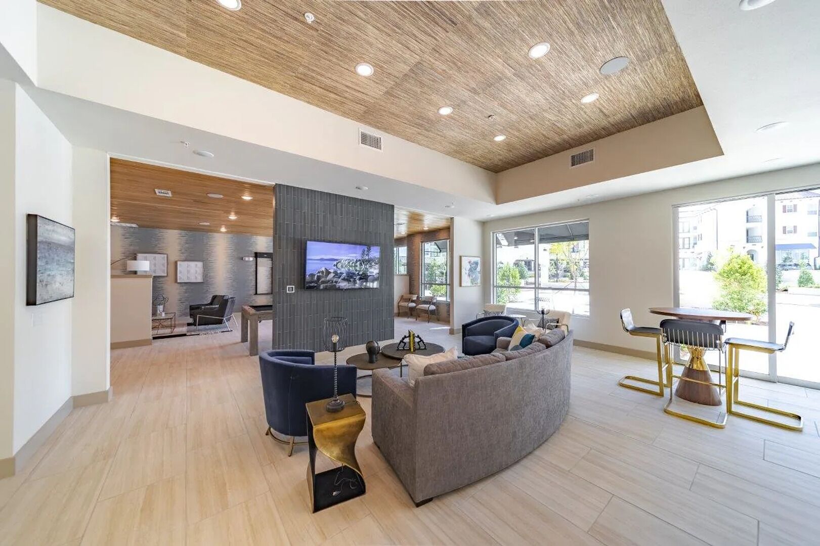 A spacious hotel lobby with a modern design, featuring a large grey sofa, a bar area, and a television mounted on the wall.