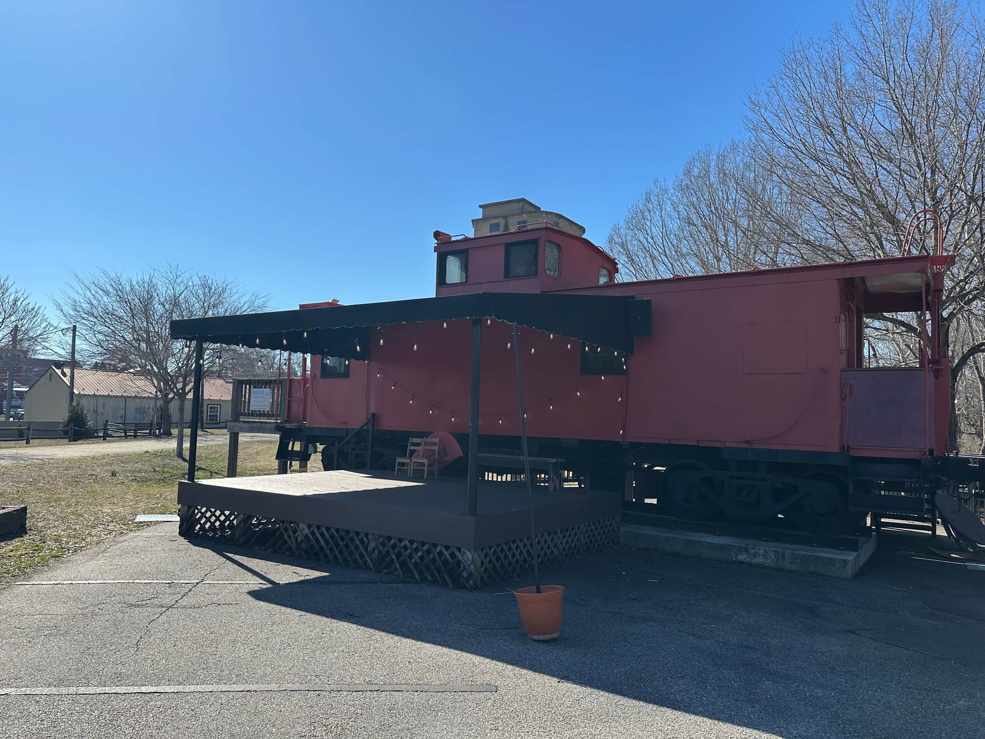 Un vagón de tren rojo con una pequeña plataforma y una planta en maceta al frente.
