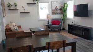 Un salon moderne comprenant une table à manger, des chaises, un canapé, un téléviseur et des plantes décoratives.