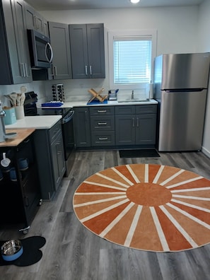 Una cocina moderna con armarios grises, un refrigerador de acero inoxidable y una alfombra redonda con un diseño de sol.