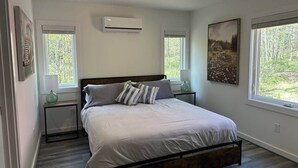 Une chambre à coucher comprenant un lit, deux tables de chevet, une fenêtre et un appareil de climatisation.