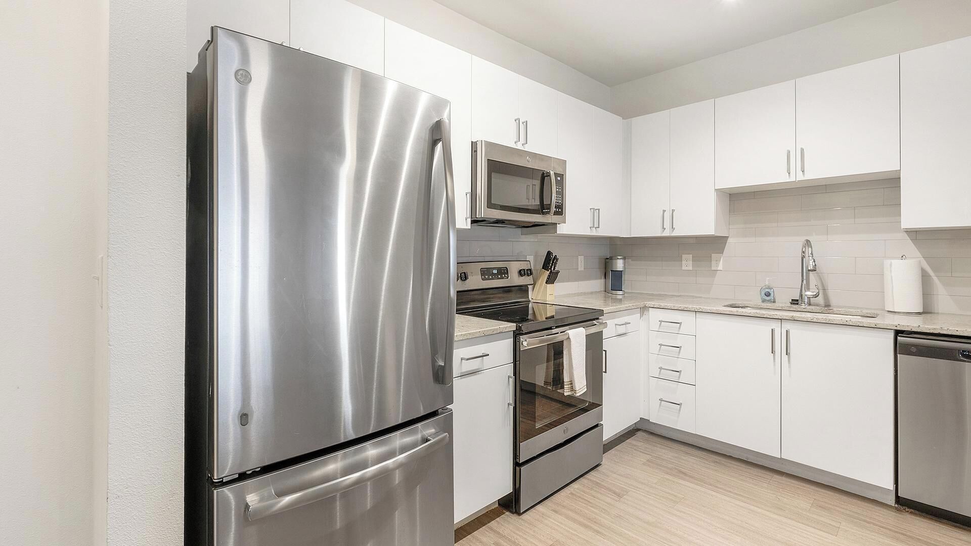 A modern kitchen with stainless steel appliances, white cabinetry, and a tiled backsplash.