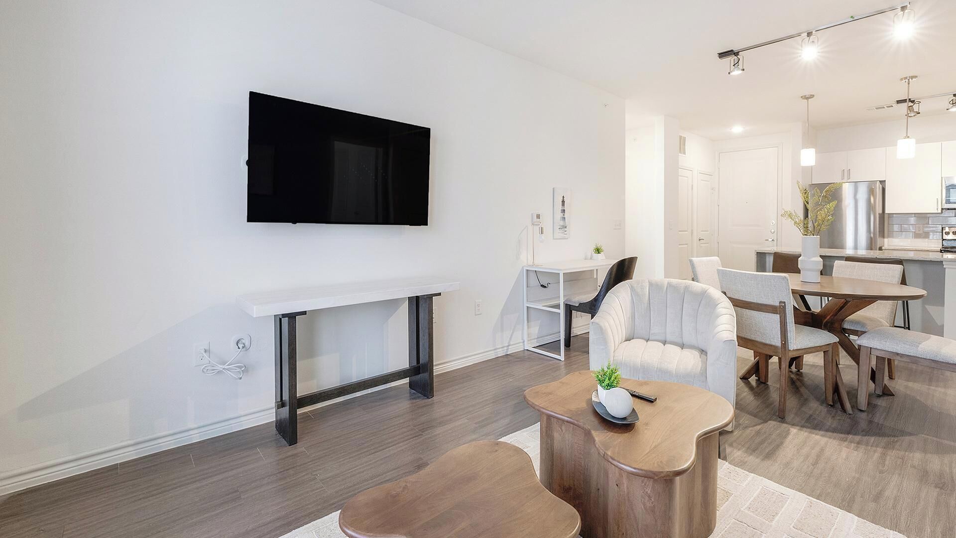 Een moderne woonkamer met een flatscreen televisie, een witte consoles, een houten salontafel en een eethoek met een witte stoel en een houten tafel.
