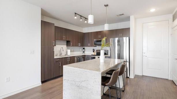 Una cocina moderna con gabinetes de madera oscura, electrodomésticos de acero inoxidable y una isla central con taburetes de bar.