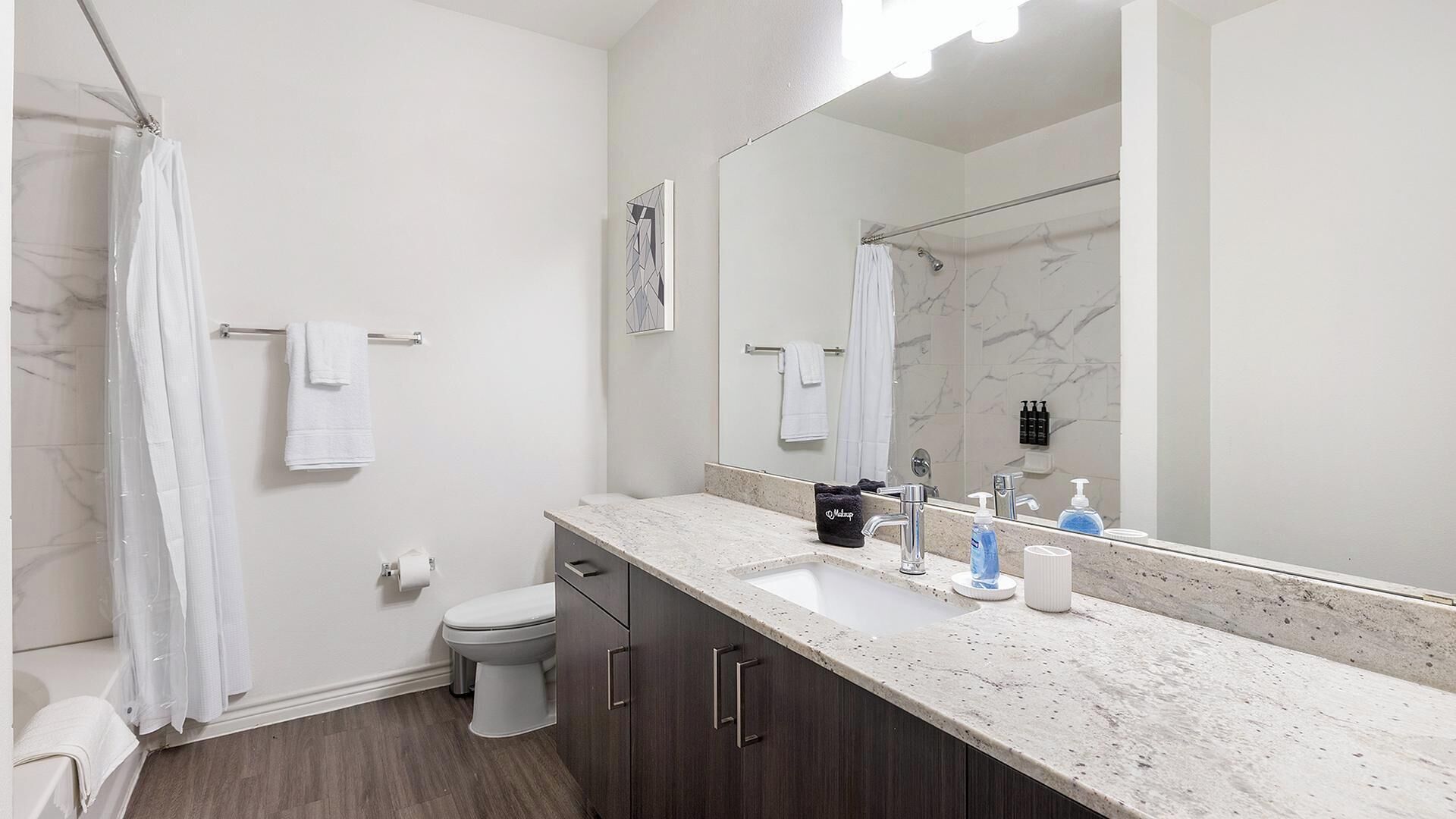 A modern bathroom with a shower, toilet, vanity, and a large mirror.