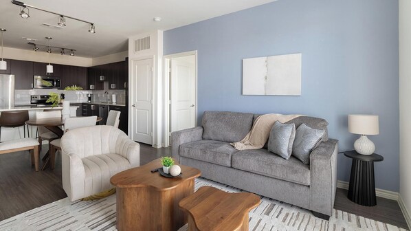 Ein modernes Wohnzimmer mit einem grauen Sofa, einem Holztisch und einem Essbereich mit einem weißen Stuhl.