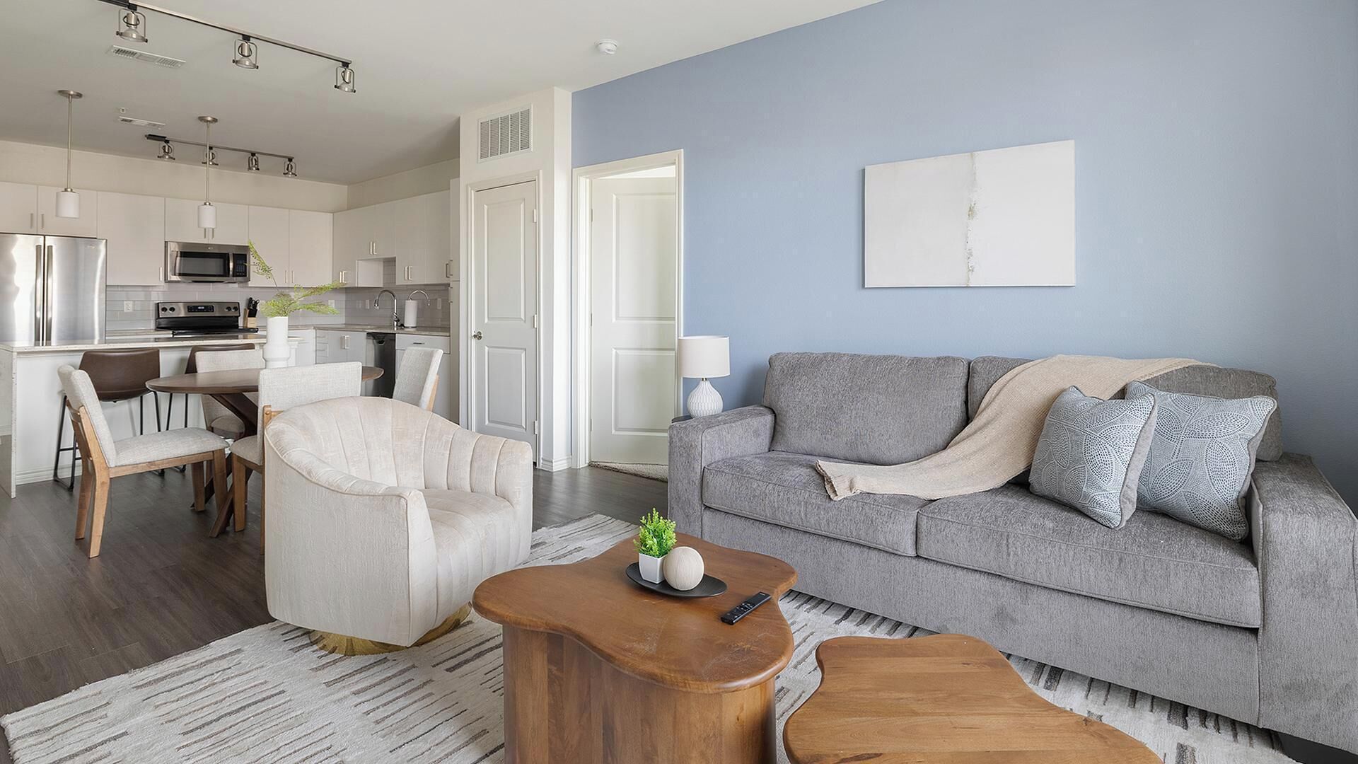 Ein modernes Wohnzimmer mit grauem Sofa, einem Holztisch und einem Essbereich mit weißem Tisch und Stühlen.