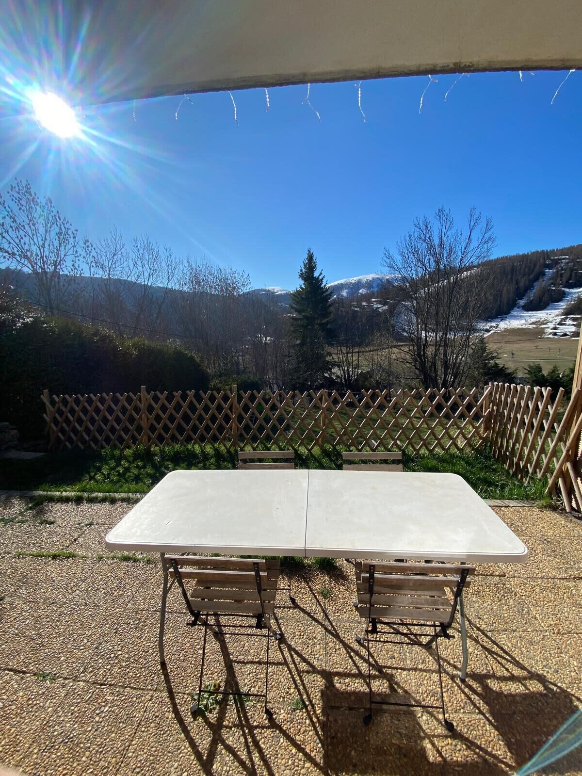 A patio with a table and chairs, a wooden fence, and a view of a snowy mountain landscape.