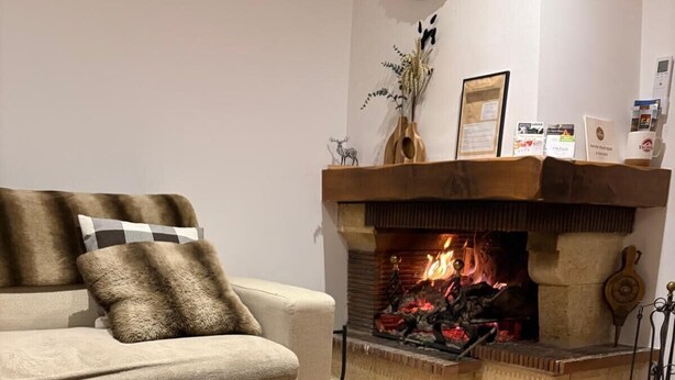Ein gemütliches Wohnzimmer mit Kamin, einem Holztisch mit Speisen, einer Couch und einem flauschigen Hocker.