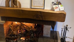 Eine hölzerne Bank mit einem dekorativen Willkommensschild, ein kleiner Tisch mit Broschüren und ein Kamin mit Holzscheiten.