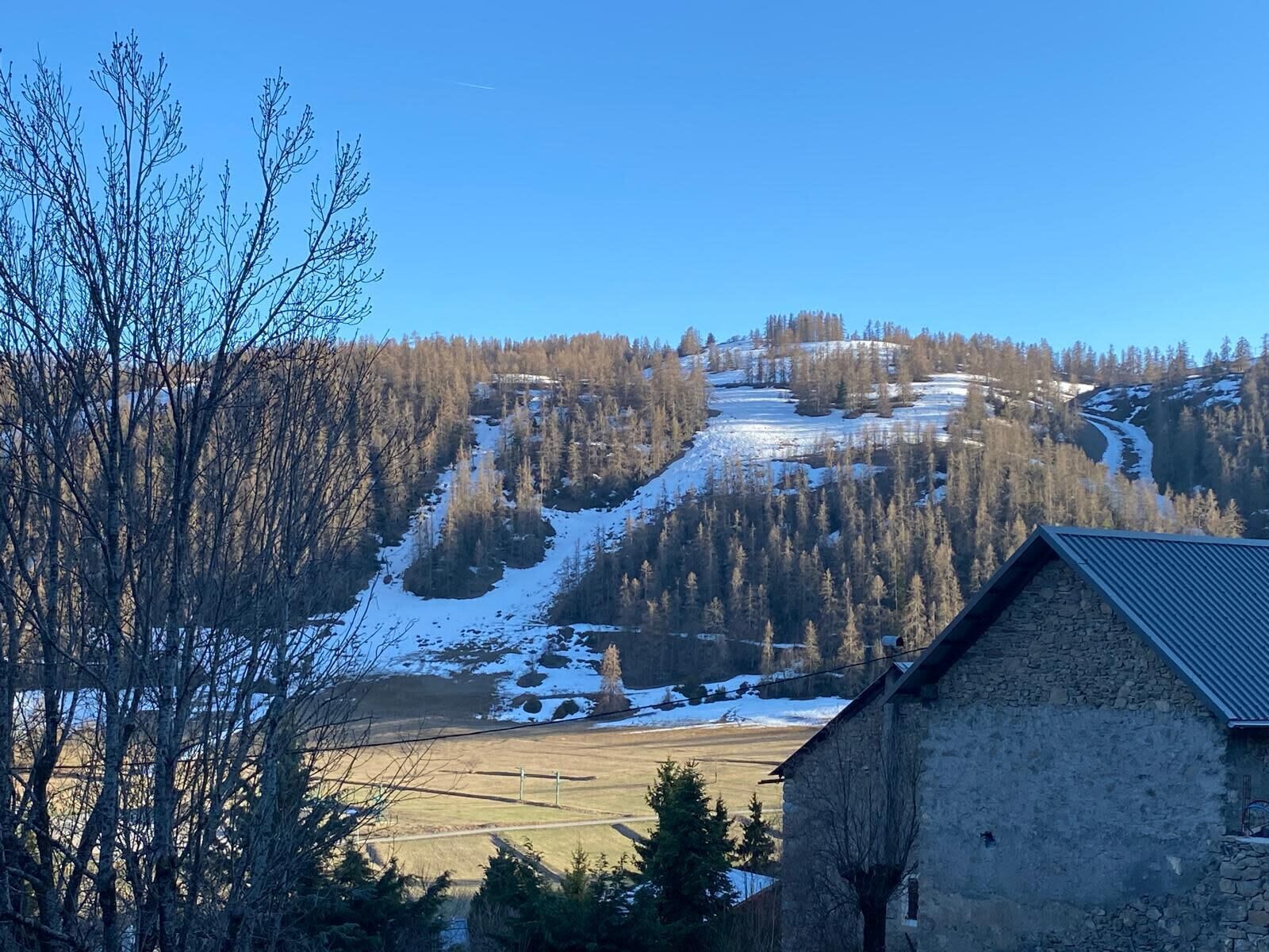 Un edificio de piedra con techo inclinado, rodeado de zona boscosa con parches de nieve.