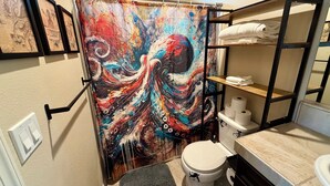 A bathroom with a colorful shower curtain, a toilet, a shelf with towels, and a rack with towels.