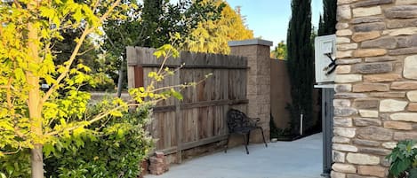 A curved concrete pathway leading to a wooden fence, surrounded by red mulch and greenery.