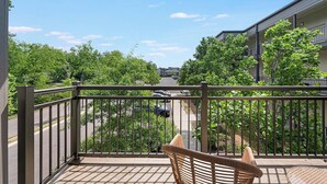 Ein Balkon mit Korbstuhl, Blick auf eine Straße und ein Gebäude im Hintergrund.