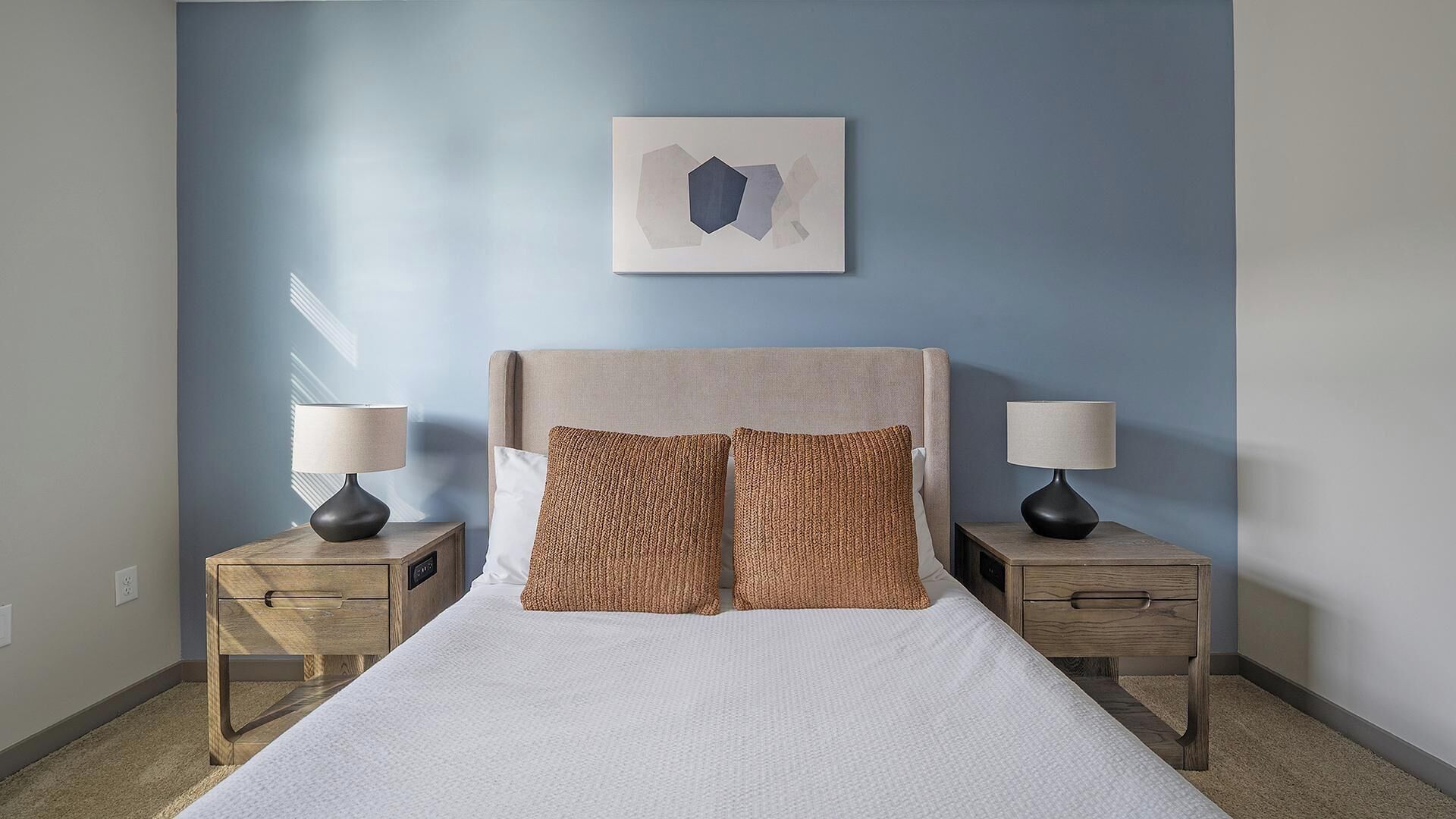 Een slaapkamer met een bed, twee nachtkastjes, twee lampen en een kunstwerk aan de muur.