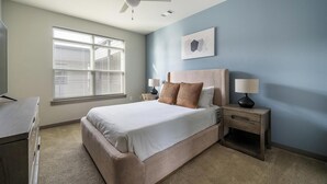 Ein Schlafzimmer mit Bett, Nachttischen, Deckenventilator, Fenster mit Jalousien und einem Wandbild.