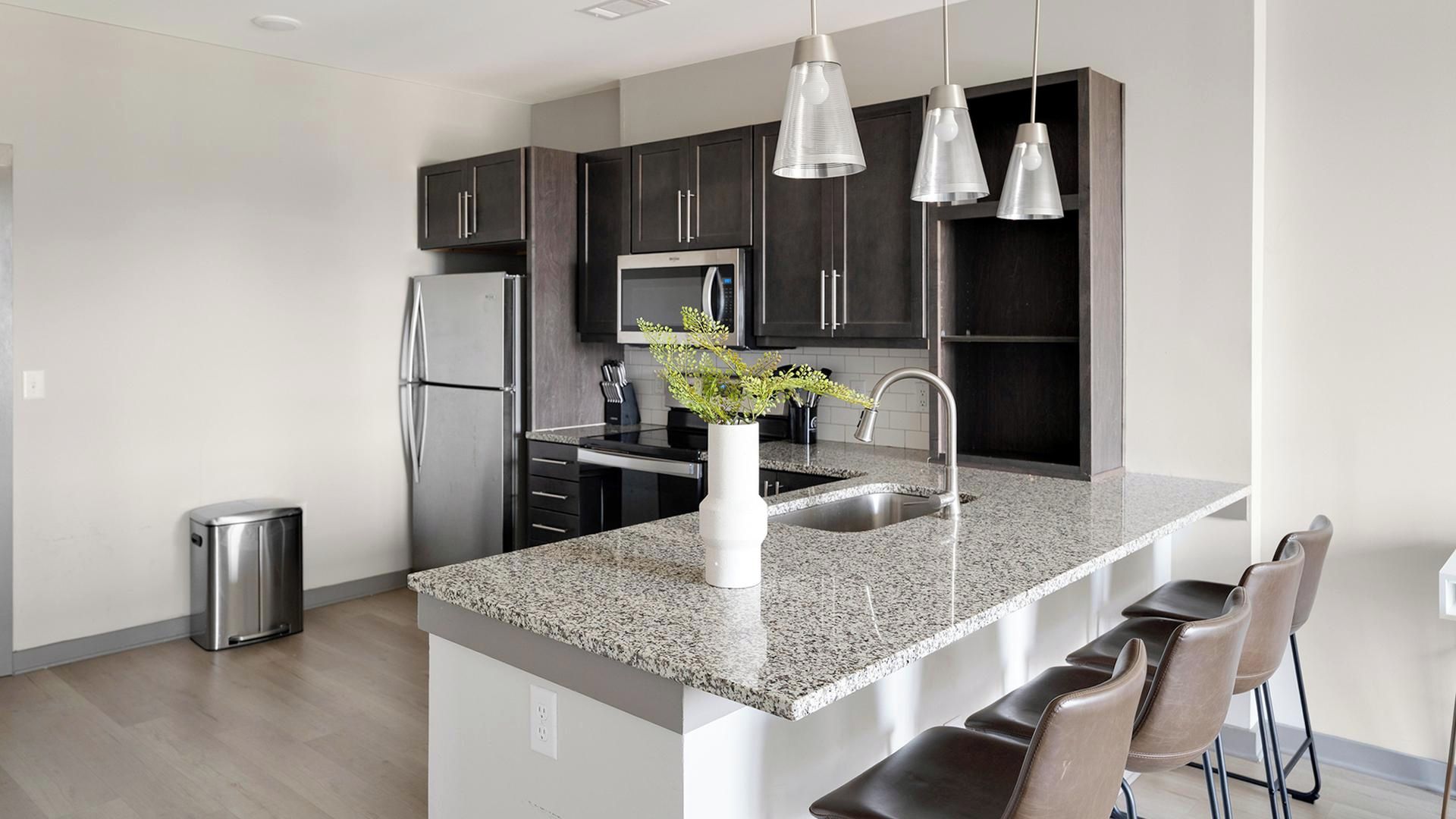 A modern kitchen with granite countertops, stainless steel appliances, and dark cabinetry.