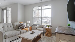 A modern living room with a grey sofa, a coffee table, a side table, a chair, and a TV mounted on the wall. - Landing | Stylish 1BD, Gym, Clubhouse (Nashville)
