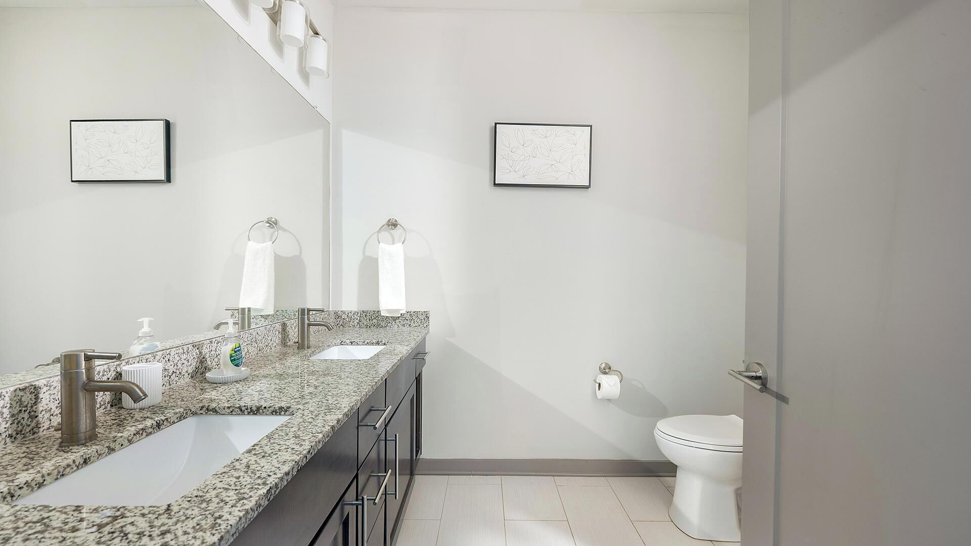 Un bagno moderno con un piano di lavoro in granito, un lavandino, un WC e due opere d'arte incorniciate a parete.