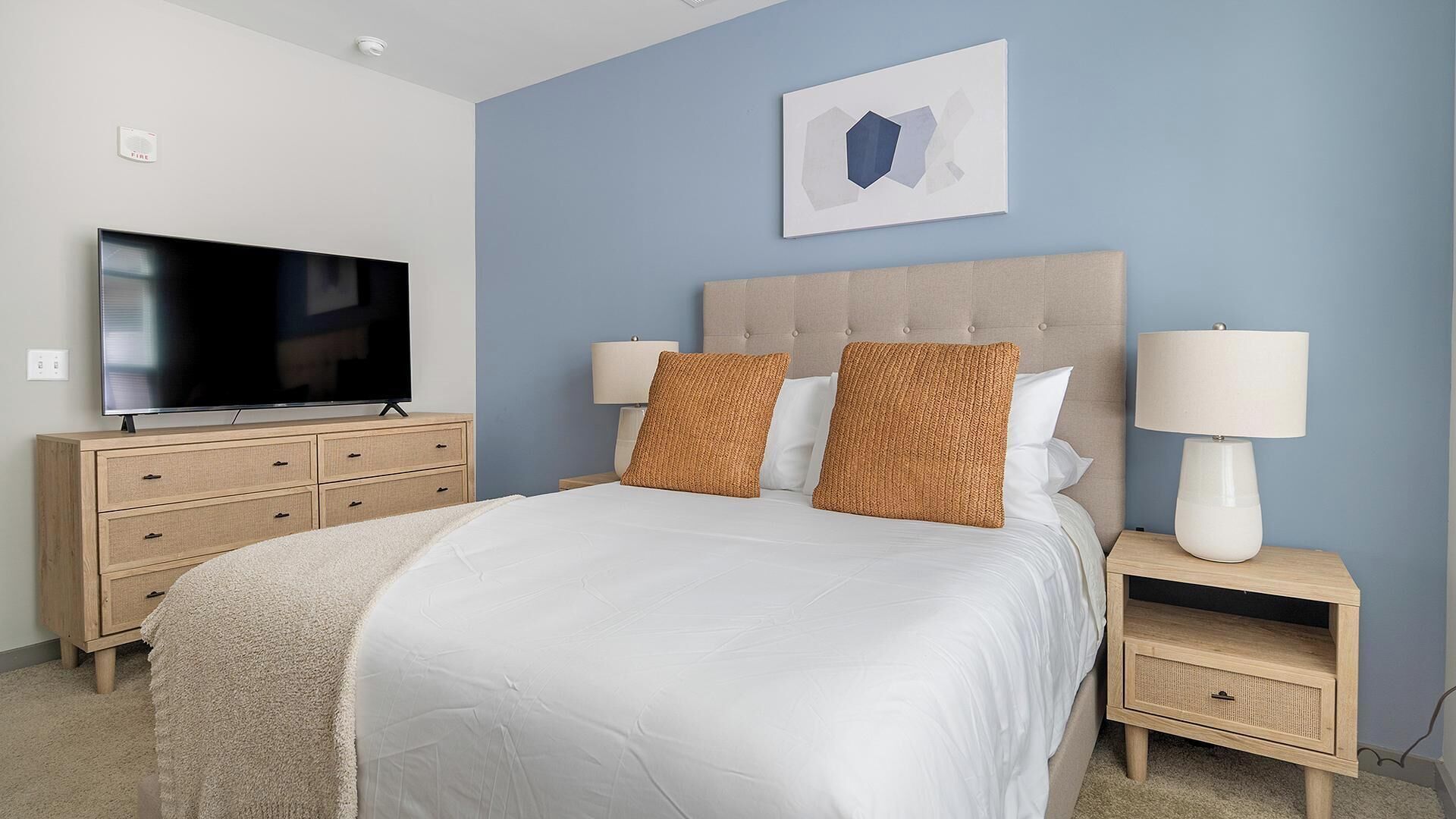 A bedroom with a bed, a TV, a bedside lamp, a nightstand, and a wall-mounted artwork.