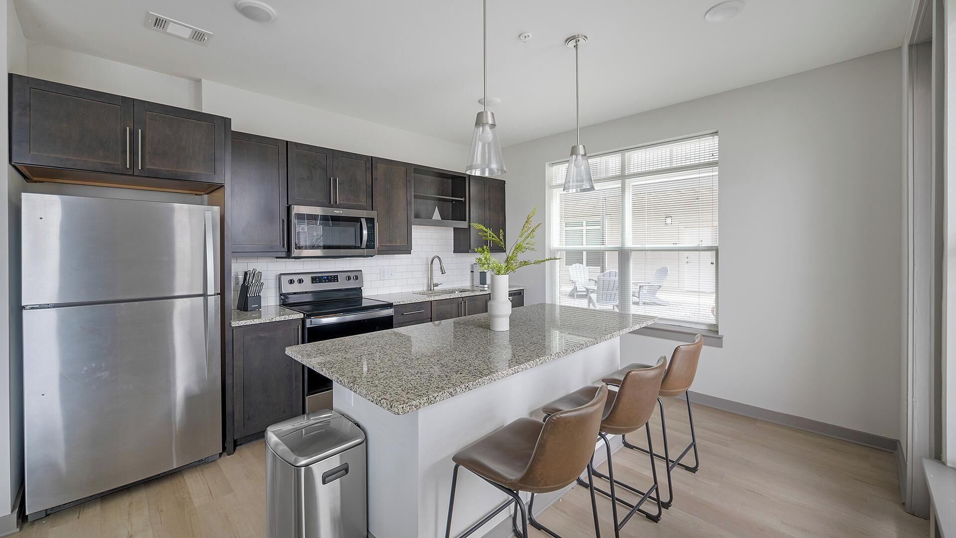 A modern kitchen with dark cabinets, stainless appliances, a granite countertop, and a central island with bar stools.