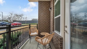 A balcony with wicker chairs, a brick wall, and a view of a street with cars. - Landing | Stylish 1BD, Gym, Clubhouse (Nashville)