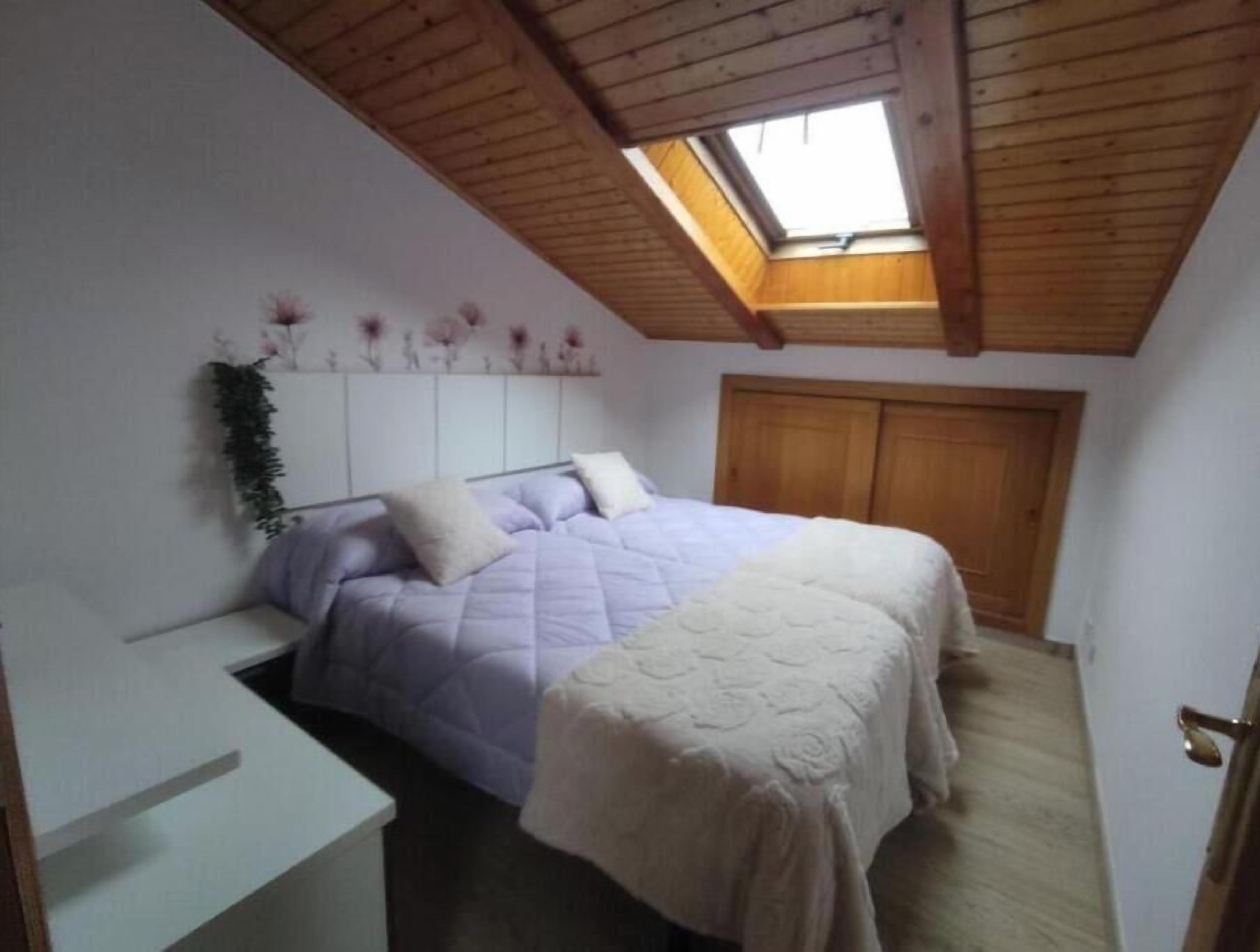 Un dormitorio con cama, escritorio, tragaluz y techo de madera.