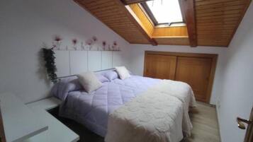 Un dormitorio con cama, escritorio, tragaluz y techo de madera.