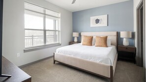 A bedroom with a large window, a bed with two pillows, two bedside tables with lamps, and a wall-mounted artwork. - Landing | Modern 1BD, Gym, Pool (Nashville)