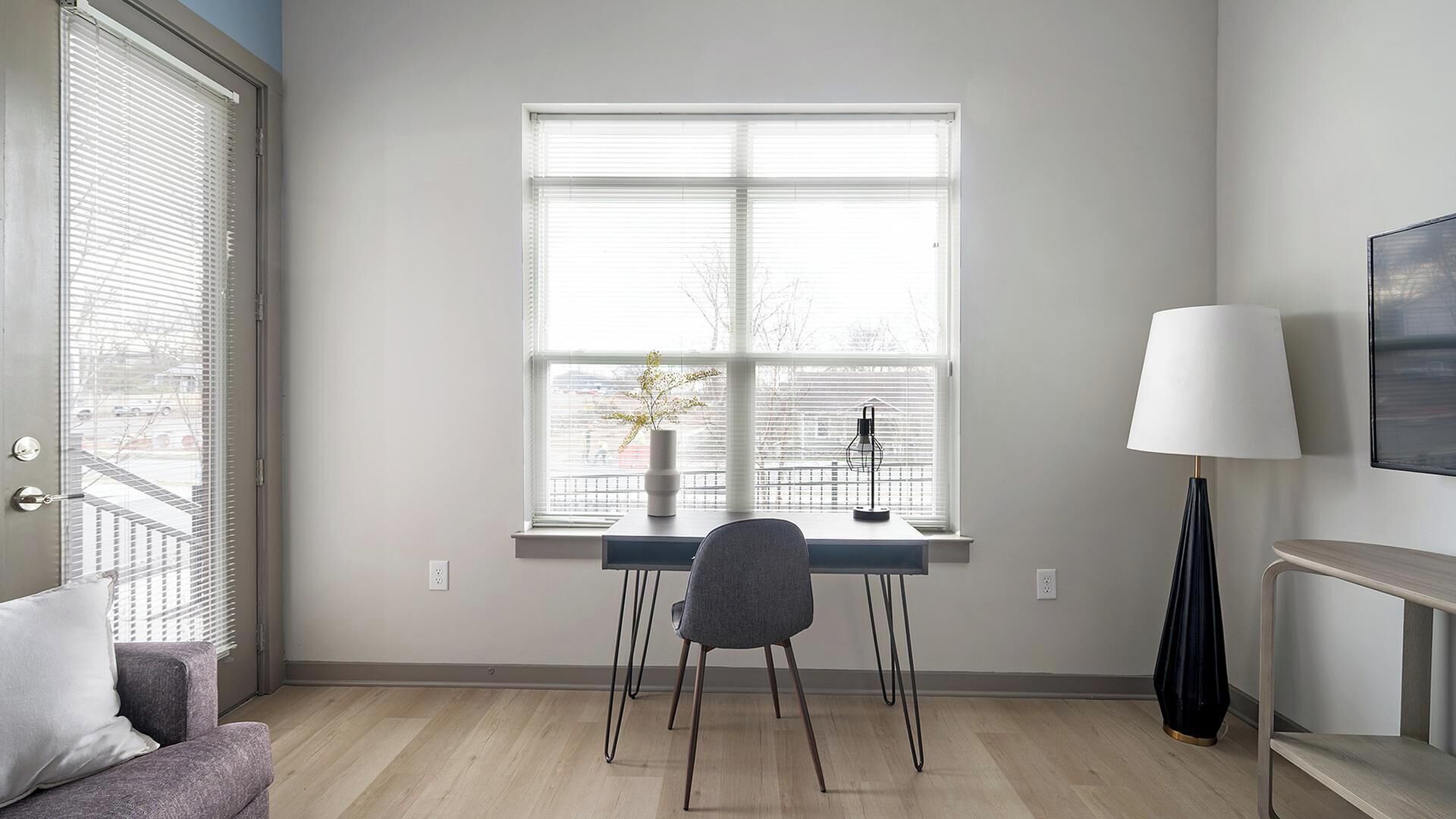 A room with a desk, chair, lamp, and a window with blinds.