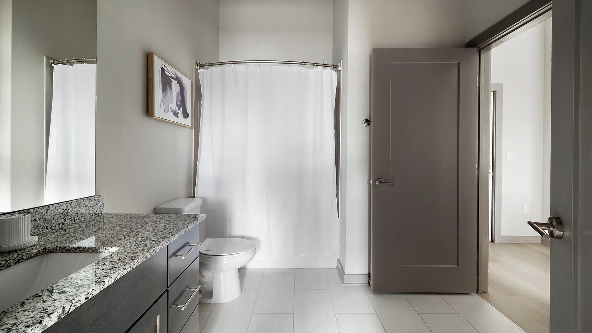 A bathroom with a granite countertop, a toilet, a shower curtain, and a door.