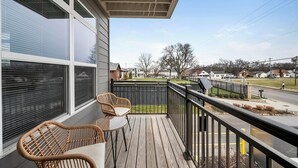 Un balcon donnant sur une rue résidentielle, une chaise en osier et une petite table.