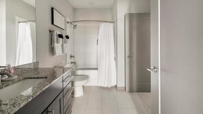 Ein modernes Badezimmer mit einer Granitplatte, einer Toilette, einer Dusche mit Glastür und einer Tür zu einem weiteren Raum.