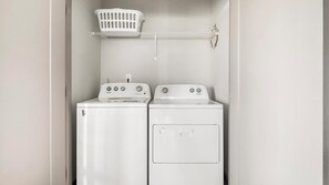 A laundry room with two white Whirlpool washers and dryers, a white laundry basket on a shelf, and a white wall. - Landing | Beautiful 2BD, Clubhouse, Gym (Nashville)