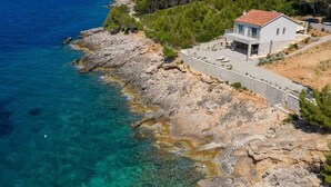 Une maison située sur la côte, avec un mur en pierre, un toit recouvert de tuiles rouges et une vue sur la mer.