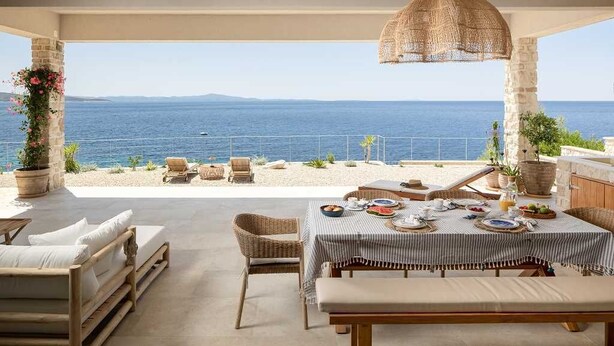 Un espace extérieur abrité, aménagé pour les repas, avec vue sur la mer, et comprenant une table, des chaises et un canapé.