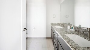 Ein modernes Badezimmer mit einer Granit-Arbeitsplatte, einem Edelstahl-Waschbecken und einem großen Spiegel.