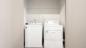 Una sala de lavandería con dos lavadoras y secadoras Whirlpool blancas, un estante metálico encima y una pared blanca.