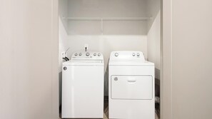 Ein Waschraum mit zwei weißen Whirlpool Waschmaschinen und Trocknern, einem Metallregal darüber und einer weißen Wand.