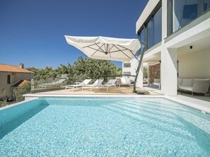 Una piscina con sillas de descanso y sombrillas, rodeada de arquitectura moderna.